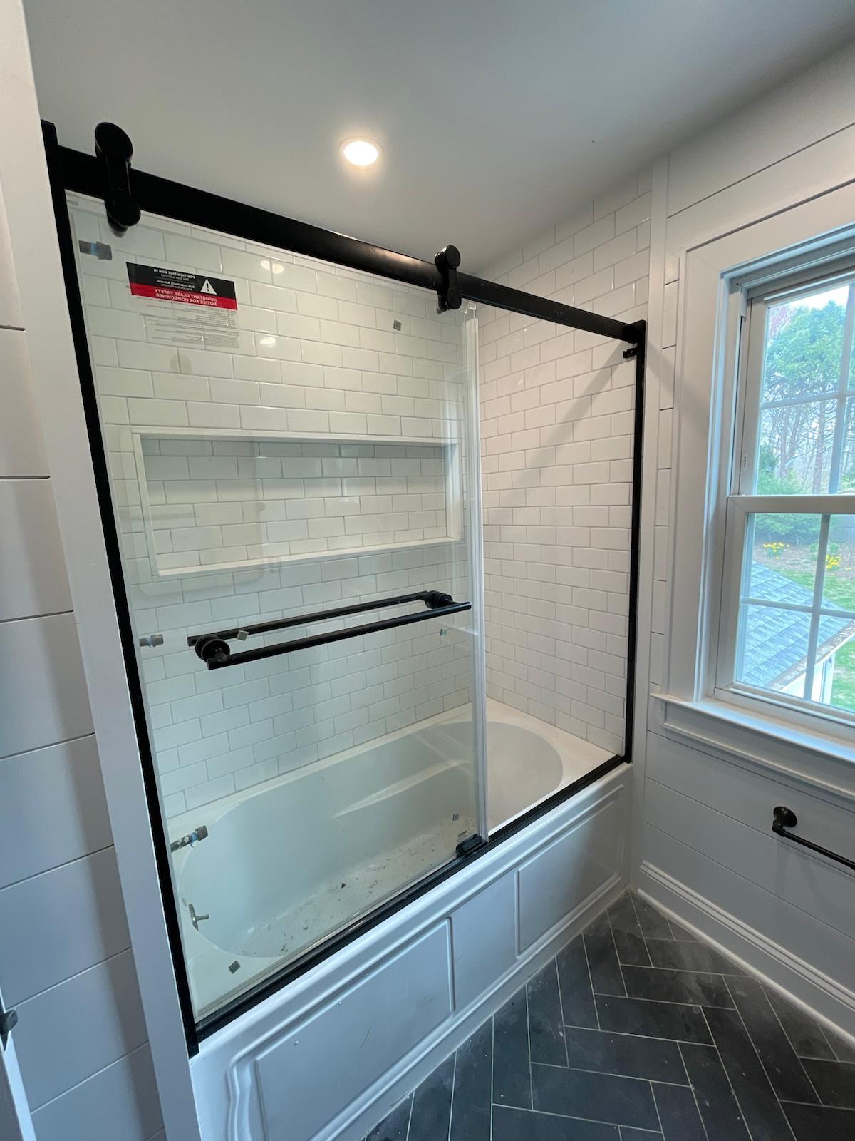 White tile bathtub and black framed sliding shower door
